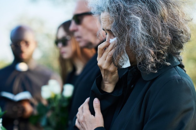 Donna anziana con i capelli grigi che asciuga le lacrime con un fazzoletto al funerale