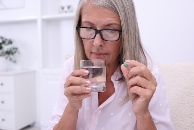Donna anziana con un bicchiere d'acqua e una pillola a casa