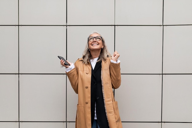 Donna anziana contenta con un sorriso sul viso con un telefono cellulare in mano