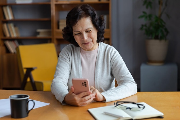 Donna anziana di mezza età europea che tiene utilizzando lo smartphone touch screen digitando scorrere la pagina elegante o