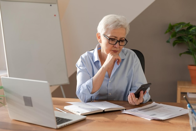 Donna anziana di mezza età europea sicura di sé che utilizza lo smartphone sul posto di lavoro