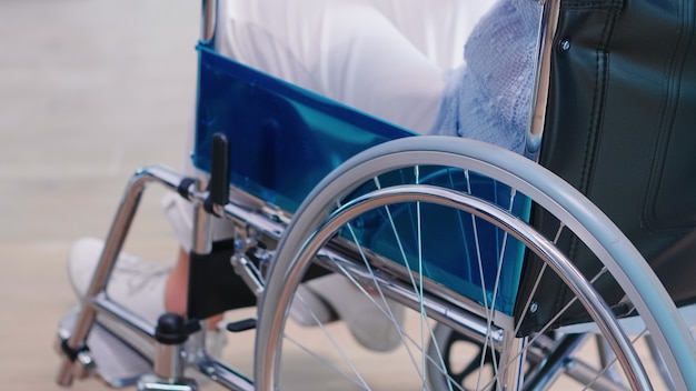 Donna anziana disabile che si tiene per mano sulla sedia wheell nel corridoio dell'ospedale. Disabilità disabilità trattamento della malattia handicappato e paralisi del paziente