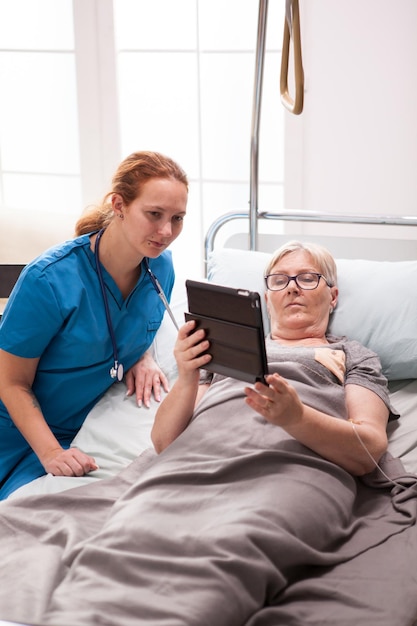 Donna anziana e dottoressa che leggono sul computer tablet. Anziana in casa di cura.