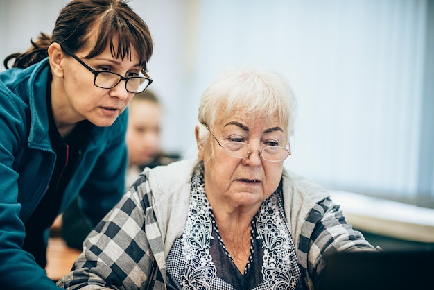 Donna anziana e insegnante seduti davanti al laptop in classe Formazione dei pensionati sulle moderne tecnologie