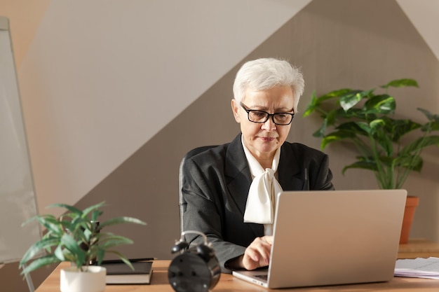 Donna anziana europea di mezza età sicura ed elegante che usa il computer portatile sul posto di lavoro