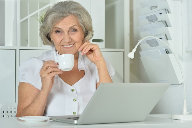 Donna anziana felice che lavora al computer portatile in ufficio