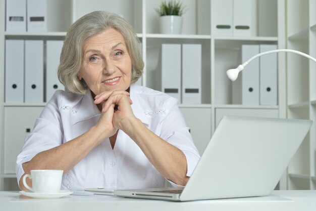 Donna anziana felice che lavora al computer portatile in ufficio