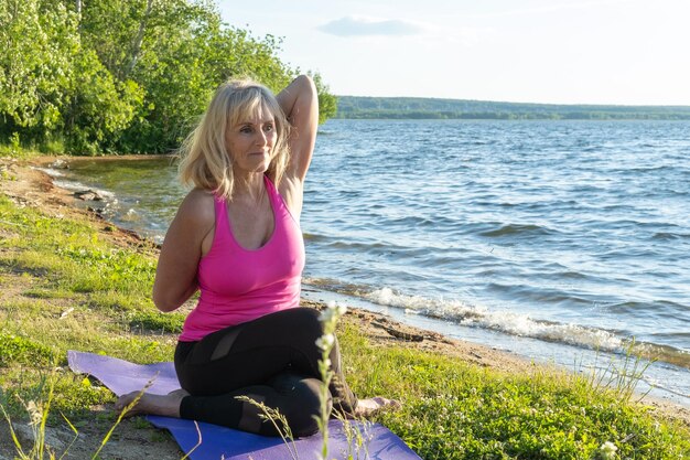 donna anziana in abiti sportivi che pratica yoga posa seduta e tenendo le mani piegate insieme