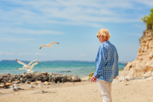 Donna anziana in piedi sulla spiaggia e guardando in lontananza