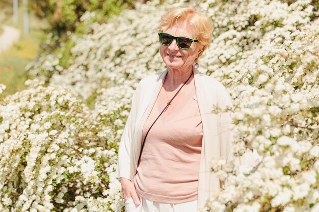 Donna anziana in posa tra cespugli con fiori bianchi