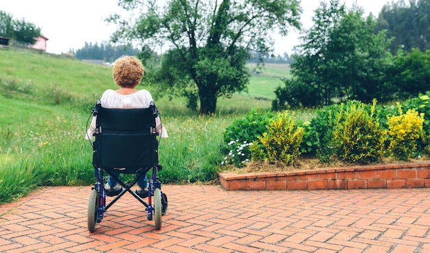 Donna anziana irriconoscibile all'indietro su una sedia a rotelle in giardino