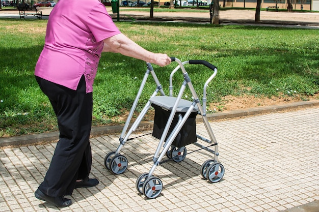 Donna anziana irriconoscibile con deambulatore che passeggia nel parco.