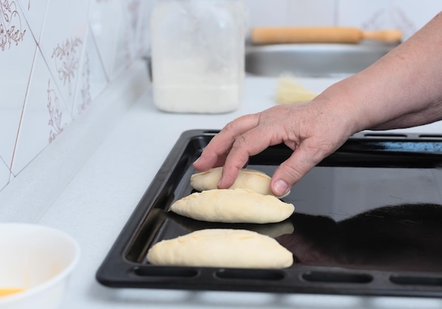 Donna anziana mani che posano torte con ripieno di mele su una teglia su un tavolo da cucina bianco Messa a fuoco selettiva Processo di preparazione di torte con ripieno di mele Cucinare a casa Concetto Cibo tradizionale