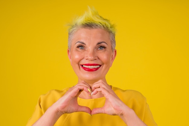 Donna anziana matura con capelli tinti di giallo alla moda colorati e labbra rossetto rosso in un vestito caldo figura del dito sentito lo studio di sfondo della carta di San Valentino.