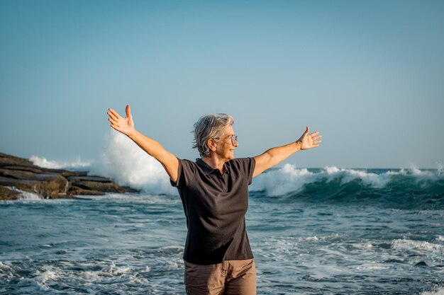 Donna anziana matura felice con le braccia tese in piedi sulla spiaggia al tramonto