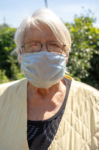 Donna anziana nel suo giardino che indossa la maschera per il viso