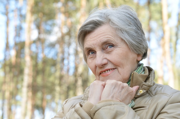 Donna anziana pensierosa che cammina nella foresta in autunno