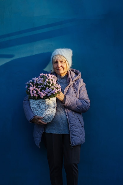 donna anziana positiva che porta fiori in vaso mentre rappresenta il concetto di hobby e giardinaggio