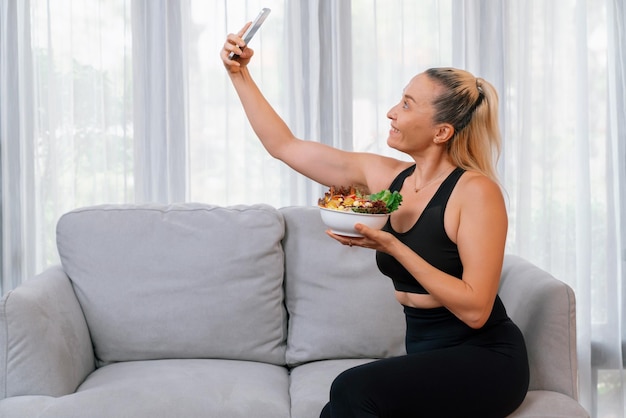 Donna anziana sana in abbigliamento sportivo che si fa selfie con lo smartphone con in mano una ciotola di frutta e verdura Stile di vita vegano e alimentazione sana per il concetto di fisico fitness corpo Peso