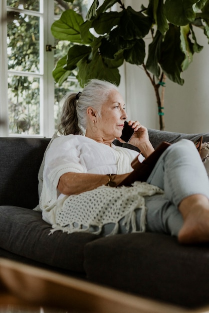 Donna anziana sdraiata e parlando al telefono su un divano