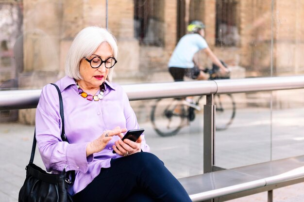 Donna anziana seduta alla fermata dell'autobus che usa il telefono