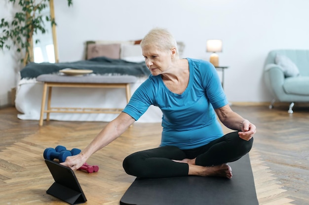 Donna anziana seduta in una posa yoga davanti a un computer portatile aperto