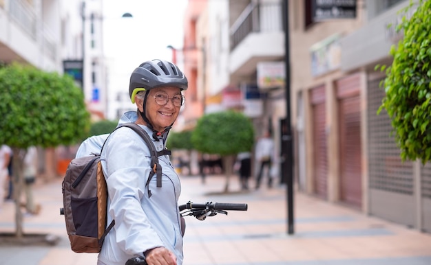 Donna anziana sorridente attraente del ciclista che corre con la bicicletta elettrica in una strada della città che esamina macchina fotografica Nonna attiva anziana che gode di uno stile di vita sano e del tempo libero in pensione