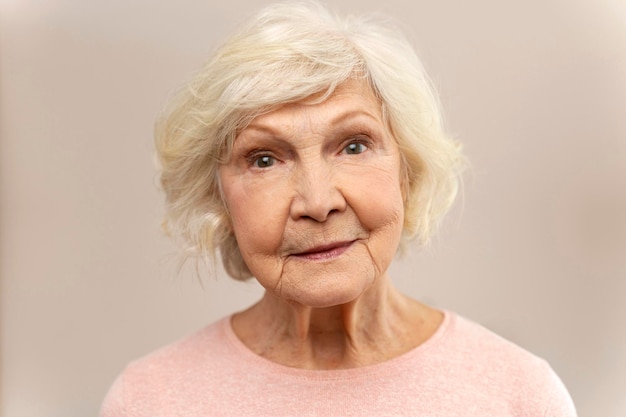 Donna anziana sorridente bionda che guarda la macchina fotografica a casa Vecchia donna anziana ritratto Pensionamento persone concetto Stock foto