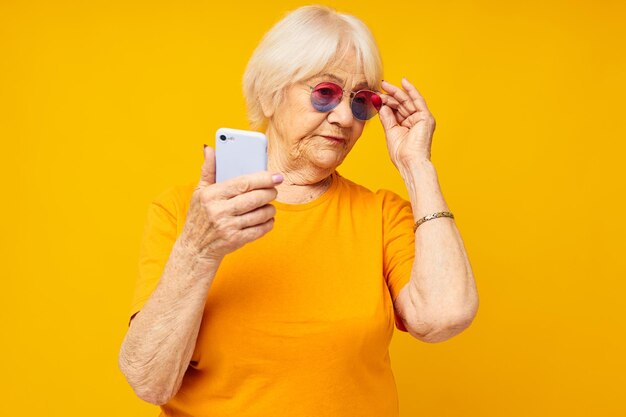 Donna anziana sorridente che parla al telefono in tecnologie di occhiali gialli