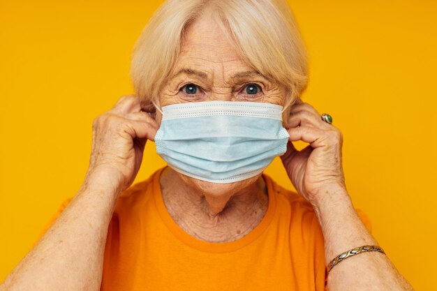 Donna anziana sorridente in maglietta casual maschera medica sfondo giallo