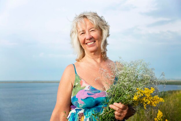 Donna anziana sorridente in un prendisole estivo con fiori in un campo Amore per la natura e il relax