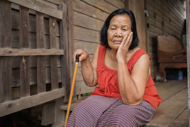Donna anziana tailandese in collare senza maniche girocollo con mal di testa e volto stressato preoccupato nella vecchia casa di legno