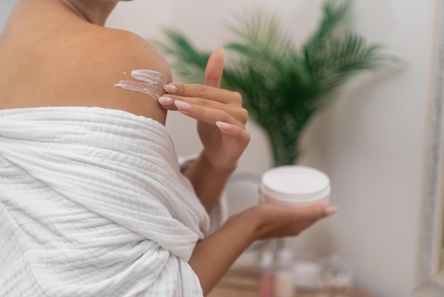 Donna applica crema per il corpo da barattolo massaggi crema idratante sulla sua spalla spa personale