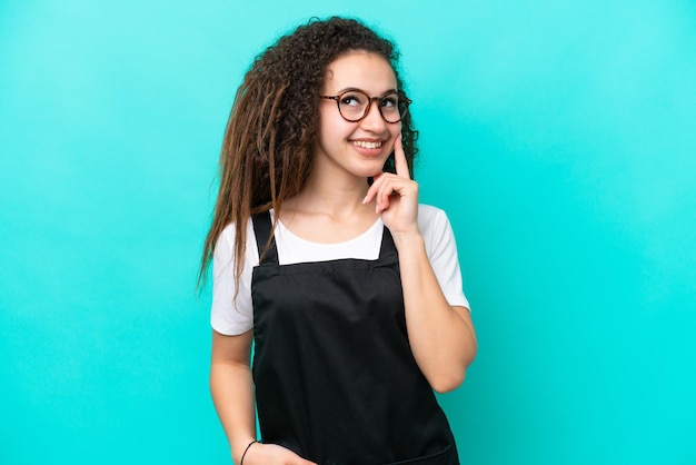 Donna araba del cameriere del ristorante isolata su fondo blu che pensa un'idea mentre osserva in su