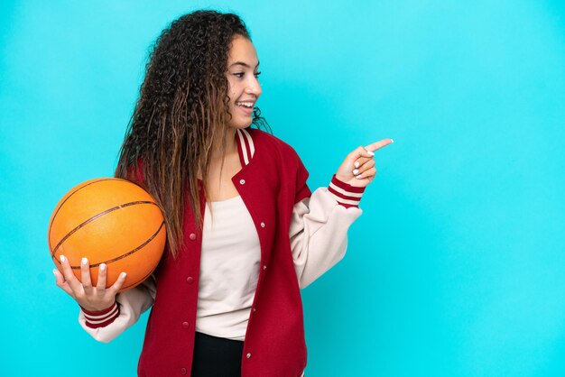 Donna araba del giocatore di basket isolata su sfondo blu che punta il dito di lato e presenta un prodotto