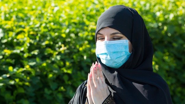 Donna araba in una sciarpa nera in testa in una maschera medica protettiva