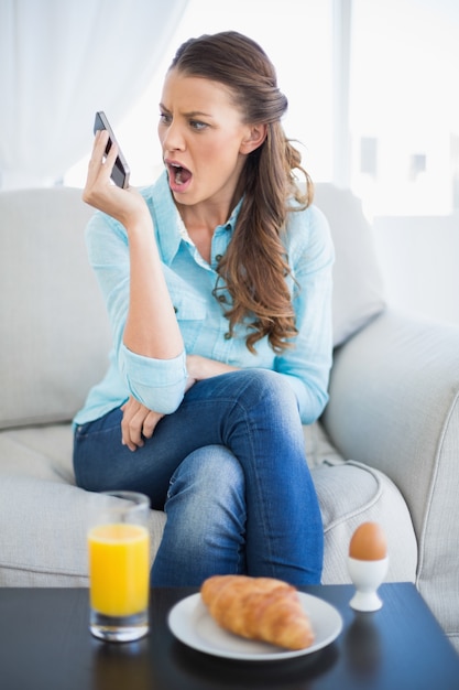 Donna arrabbiata che grida sul telefono che si siede sul sofà