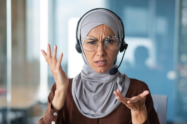 Donna arrabbiata in hijab che parla in videochiamata donna d'affari con il primo piano del telefono auricolare guardando il web