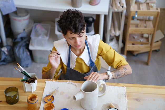 Donna artigiana in studio di ceramica disegno su argilla teiera fatta a mano ceramista femminile al lavoro