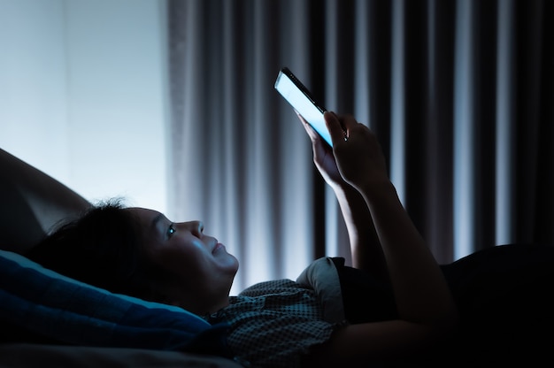 Donna asiatica a letto a tarda notte e utilizza lo smartphone mobile prima di dormire