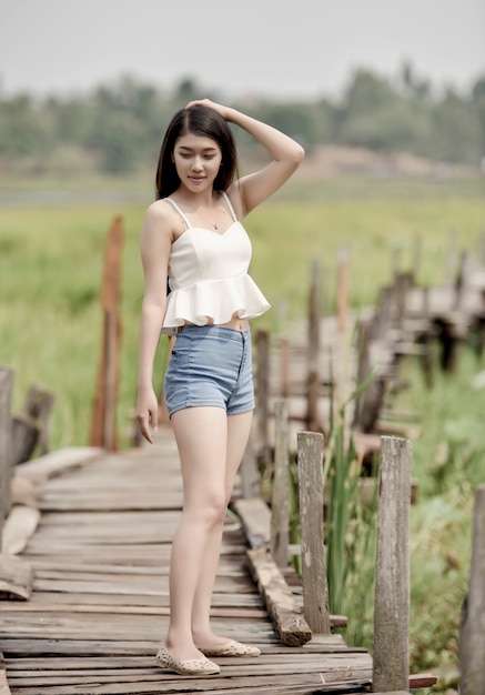 Donna asiatica abbastanza giovane che cammina sul ponte di legno