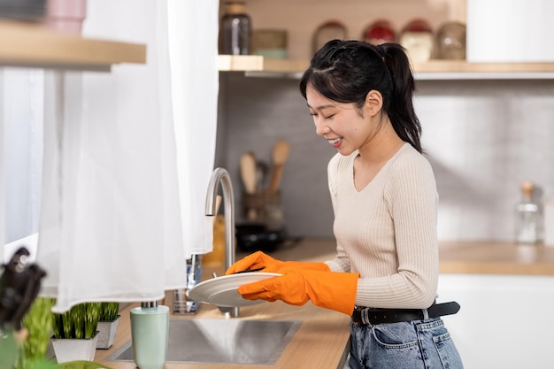 Donna asiatica allegra che lava i piatti a casa