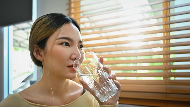 Donna asiatica assetata che beve acqua fresca e pura rinfrescante durante il giorno Stile di vita sano e concetto di idratazione