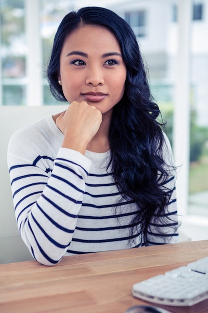 Donna asiatica attraente con il pugno sul mento che posa per la macchina fotografica in ufficio