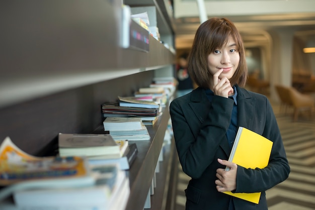 Donna asiatica attraente di affari con un libro nella libreria