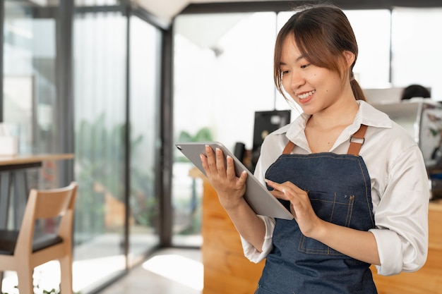 Donna asiatica barista in possesso di tablet digitale per il controllo dell'ordine dal cliente al bar caffetteria sfondo Concetto di business delle PMI