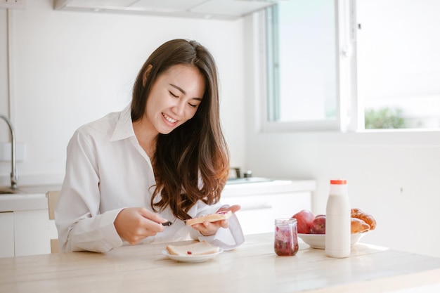 Donna asiatica che affetta il pane alla marmellata al mattino sentendosi felice e fresco Fare colazione nella stanza della cucina