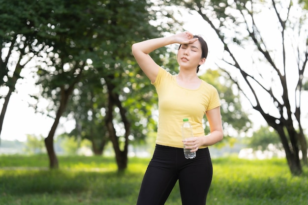 Donna asiatica che asciuga il sudore e sta per bere acqua dopo aver corso nel parco