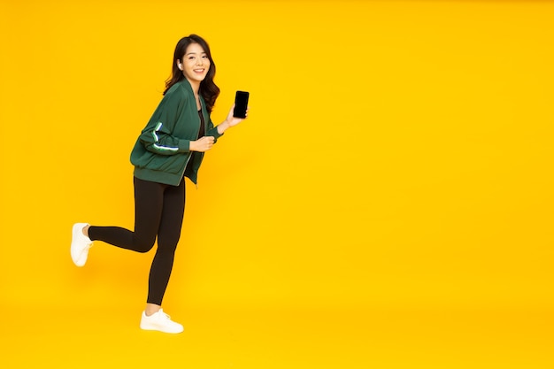 Donna asiatica che ascolta musica con auricolare wireless al telefono isolato su sfondo giallo