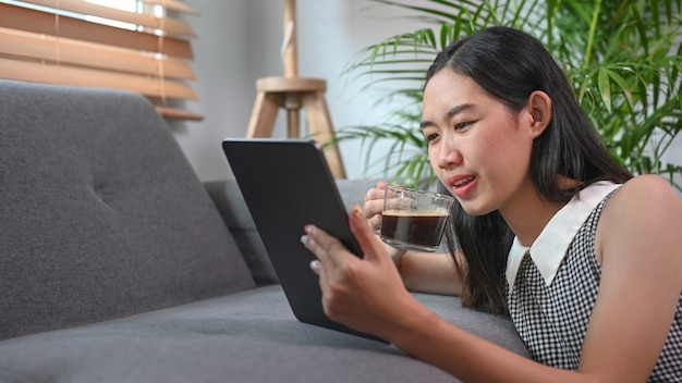 Donna asiatica che beve caffè e usa tablet in soggiorno.